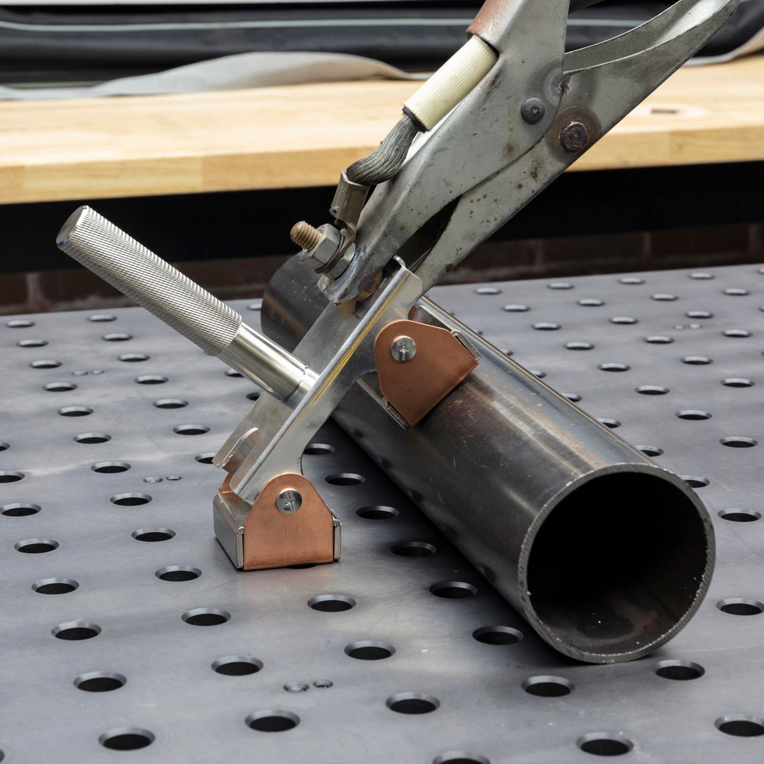 Metal pipe being held by clamps on a perforated work surface.