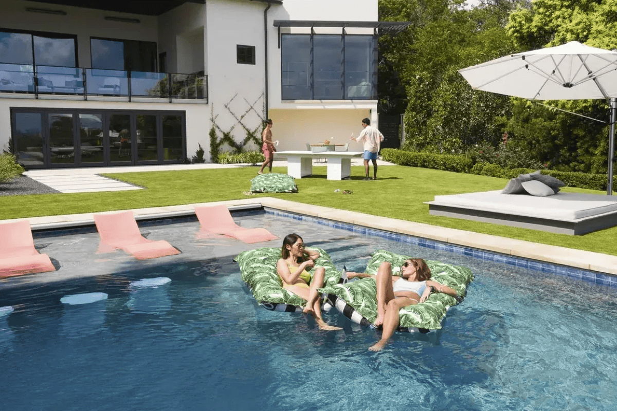 Modern backyard pool with floating loungers, in-pool chaise lounges, a shaded daybed, and outdoor entertaining areas for summer gatherings.