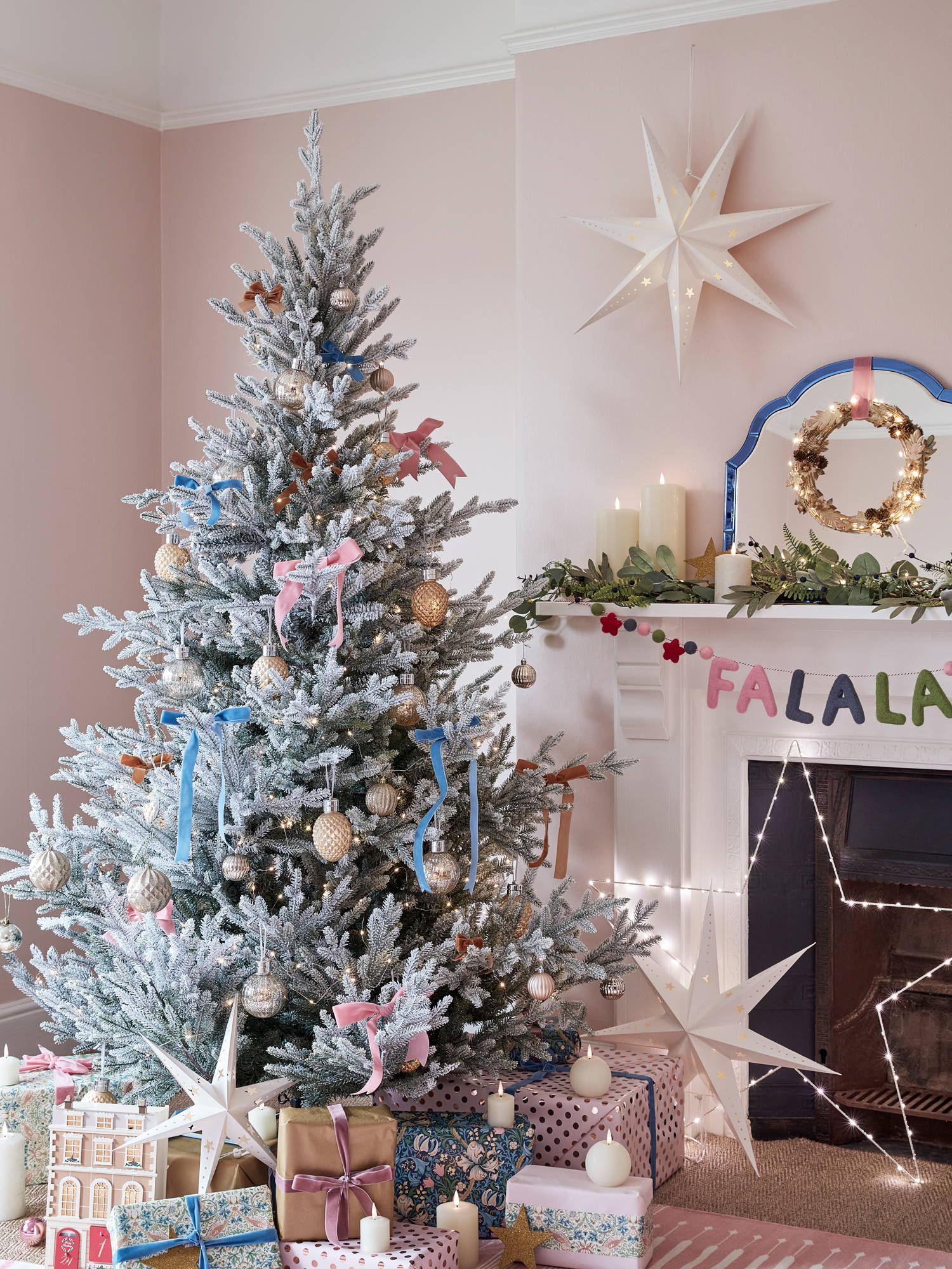 A flocked Christmas tree with colourful decorations in a pastel pink Christmas room.