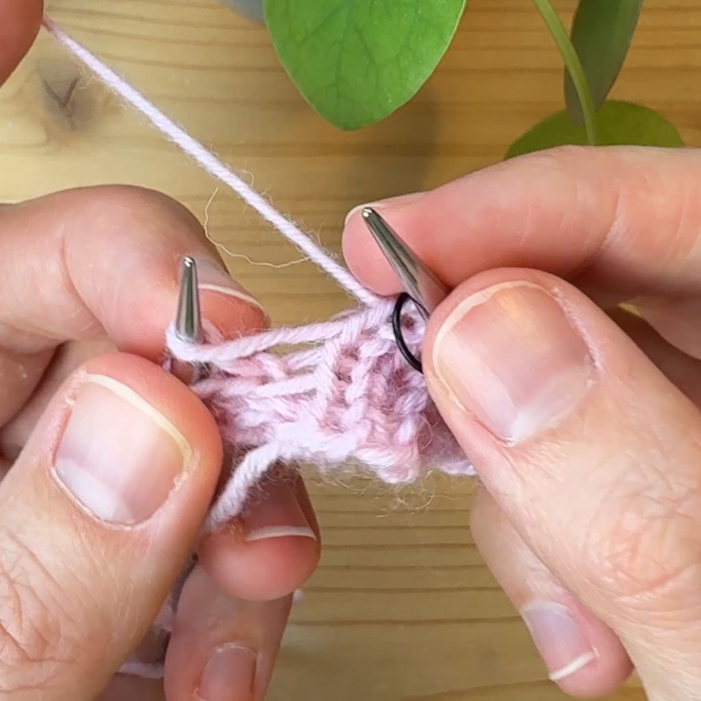 Linksgeneigte Zunahme stricken. Schritt 2.: Mit der linken Nadel von vorne unter dem Querfaden durchgehen.
