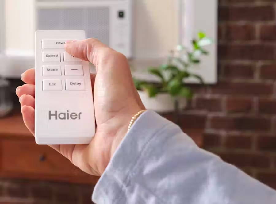 Person holding a Haier remote control for window air conditioner.