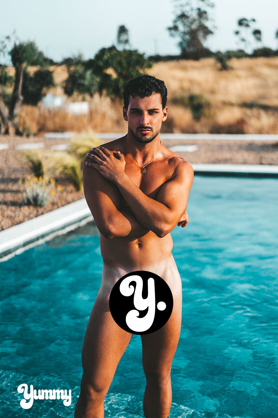 A man standing by a pool, covering himself with his arms.
