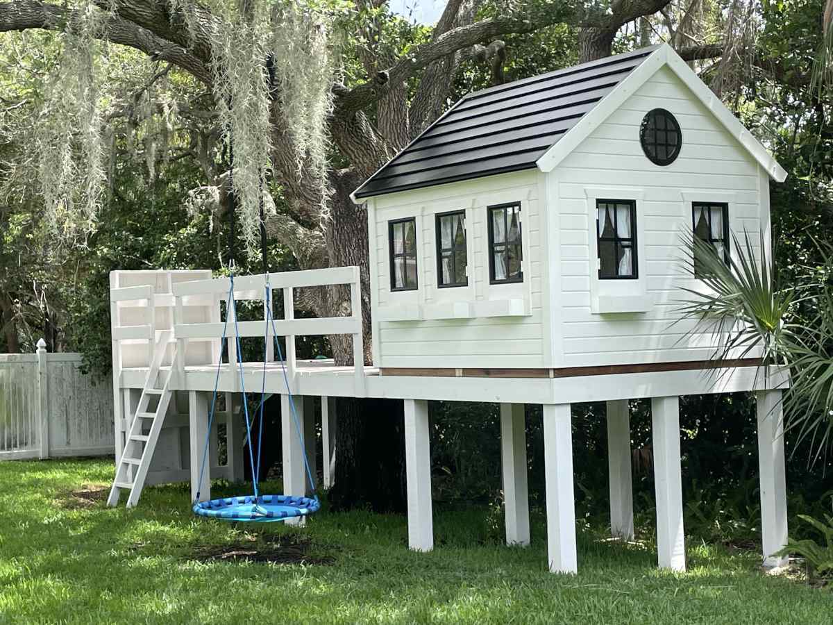 Black and white custom Wooden Playhouse with black roof and white flower boxes on stilts in a backyard by WholeWoodPlayhouses 