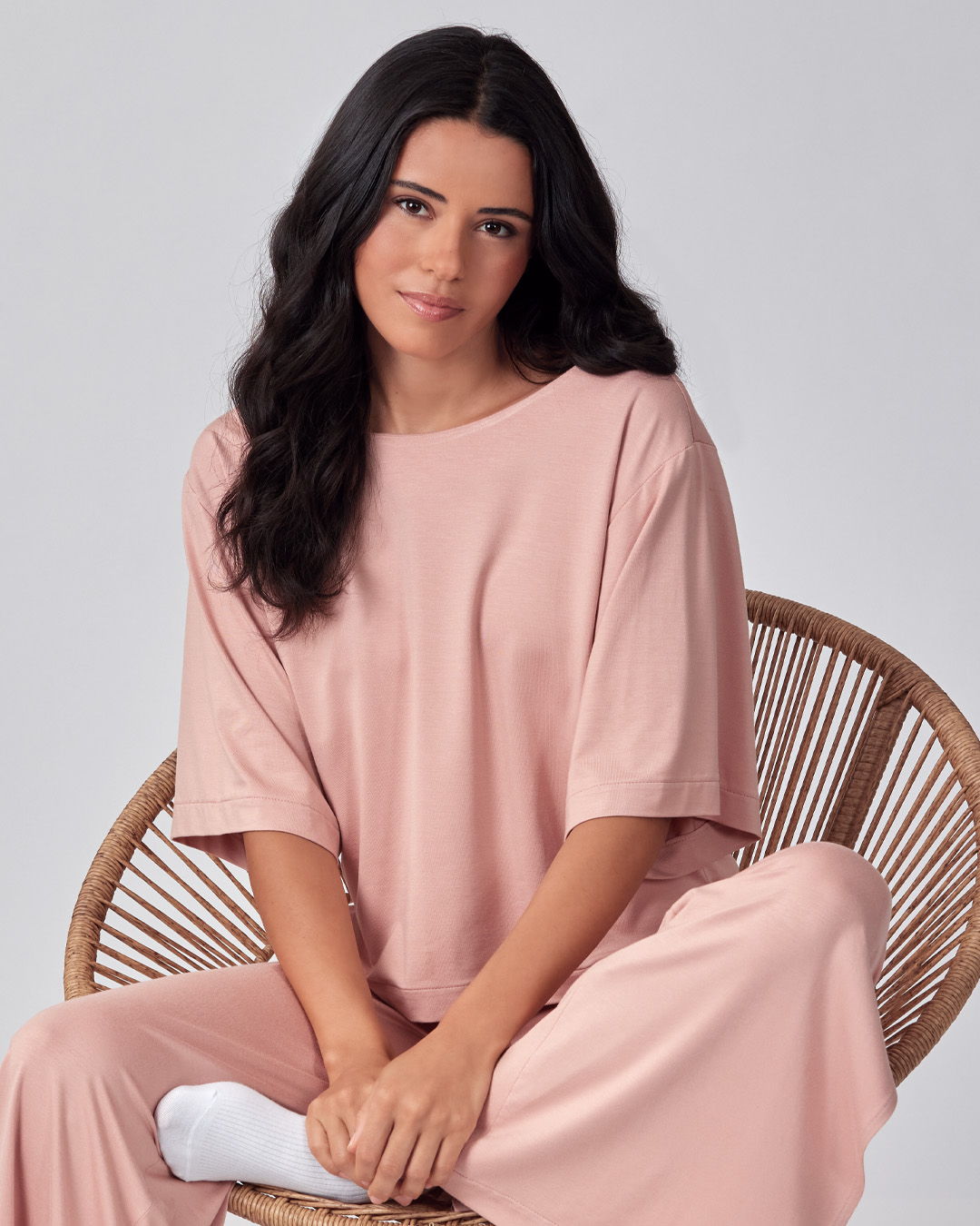 Woman in a pink outfit sitting on a rattan chair, looking at the camera.