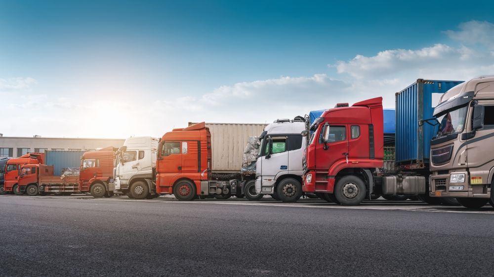 A row of trucks parked along a road under a blue sky.