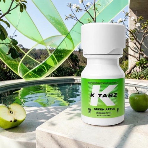 Bottle of K Tabz with green apple flavor near a pool and apples.