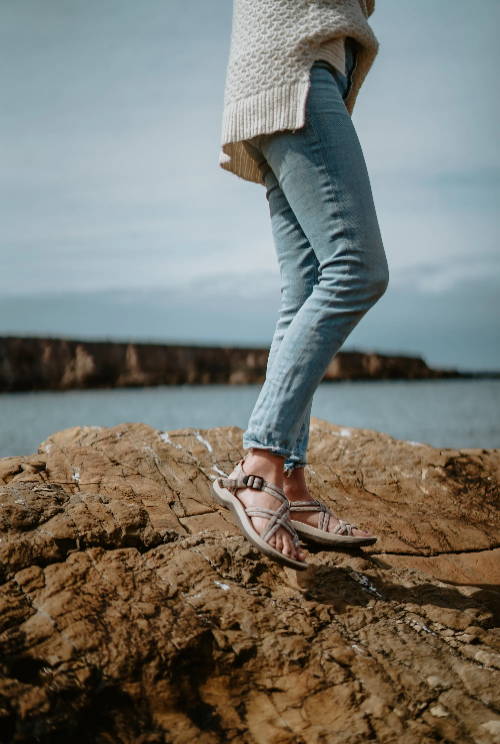 woman on rocks in jeans and athletic sandals near ocean