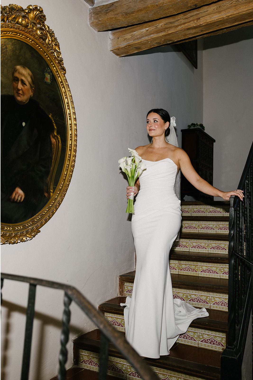 Bride in a white dress holding flowers, standing on a staircase.