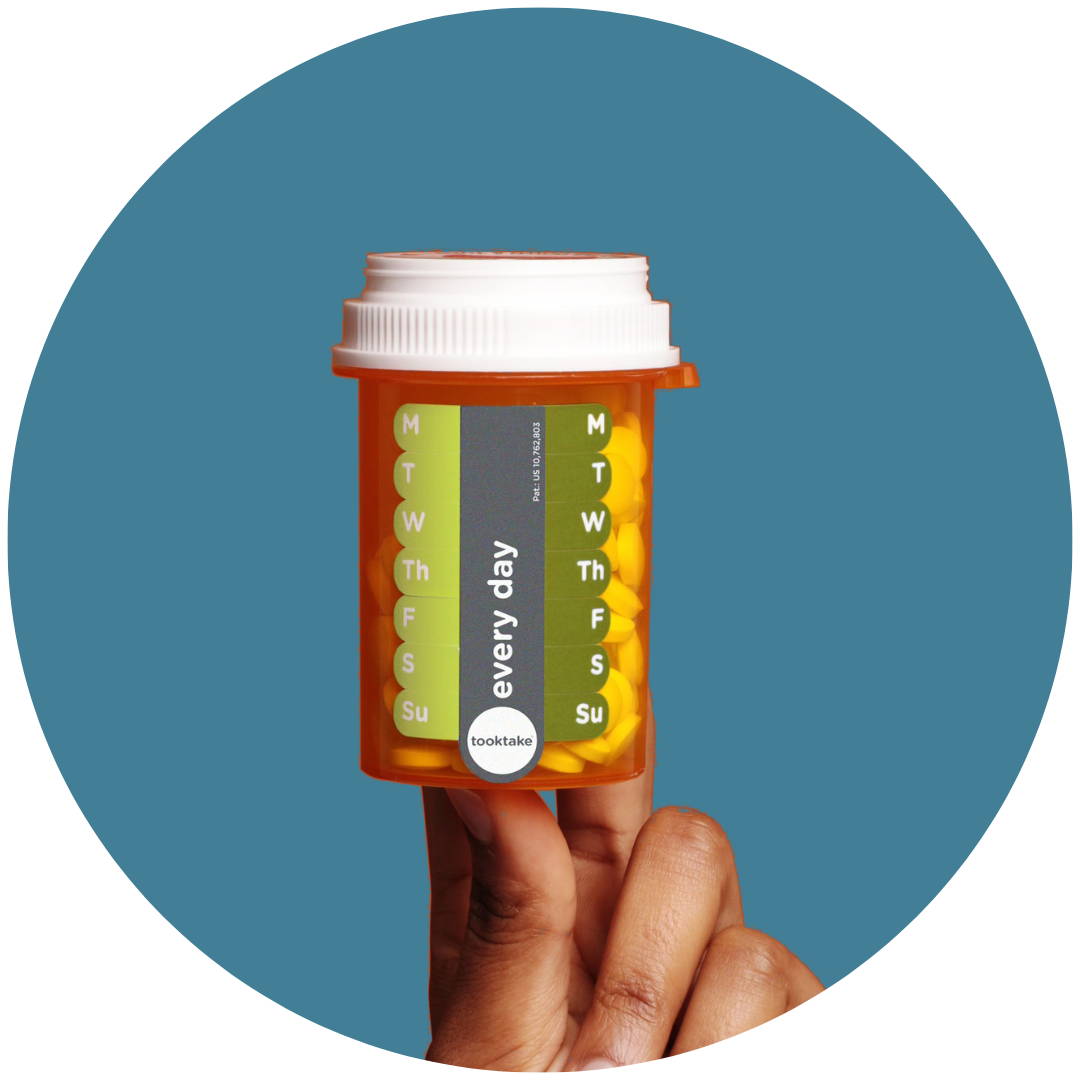 A hand holding a pill bottle with Tooktake reminder labels on it.