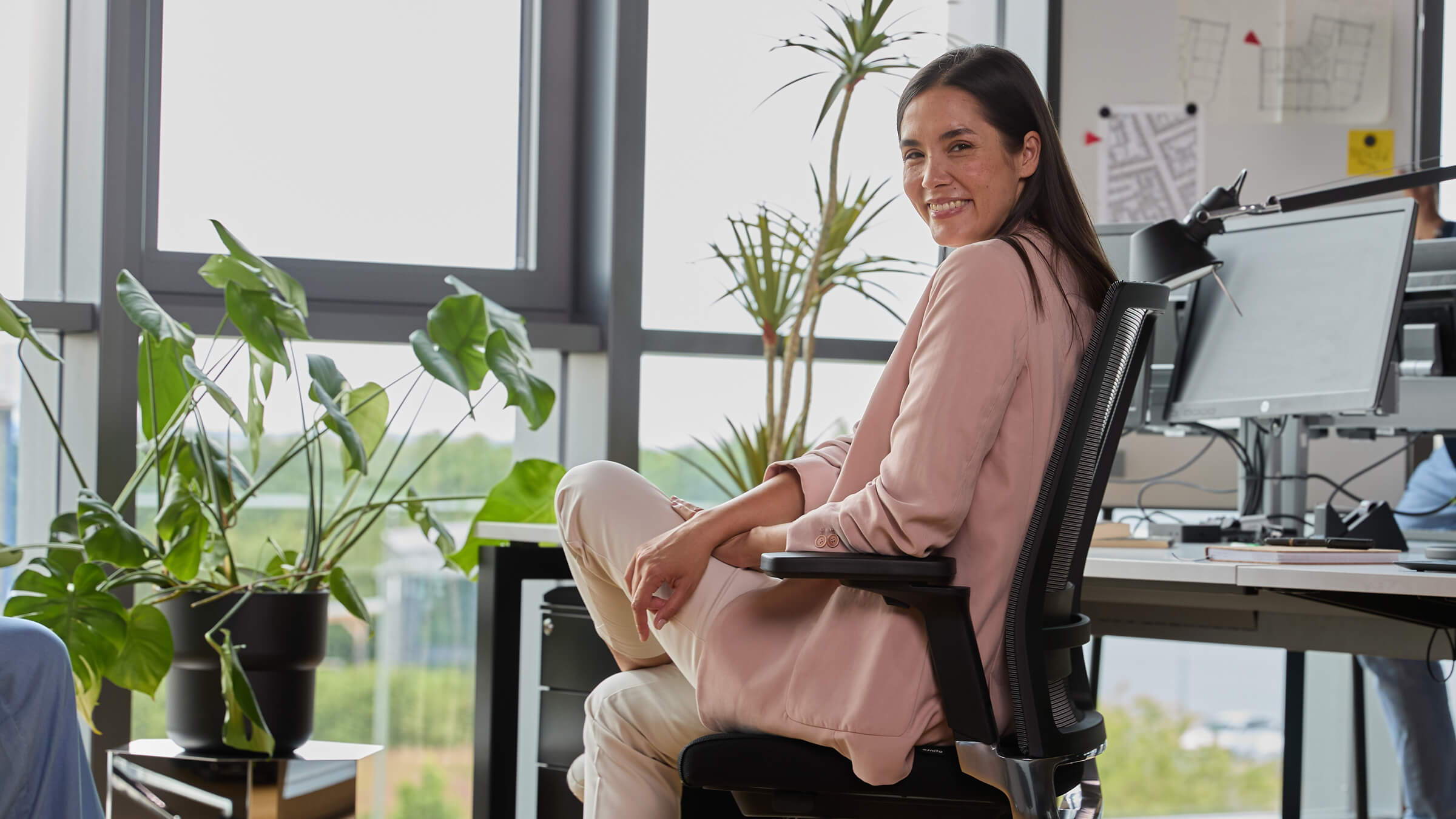 Une femme souriante est assise sur une chaise de bureau noire « Active ofinto, dans un bureau moderne