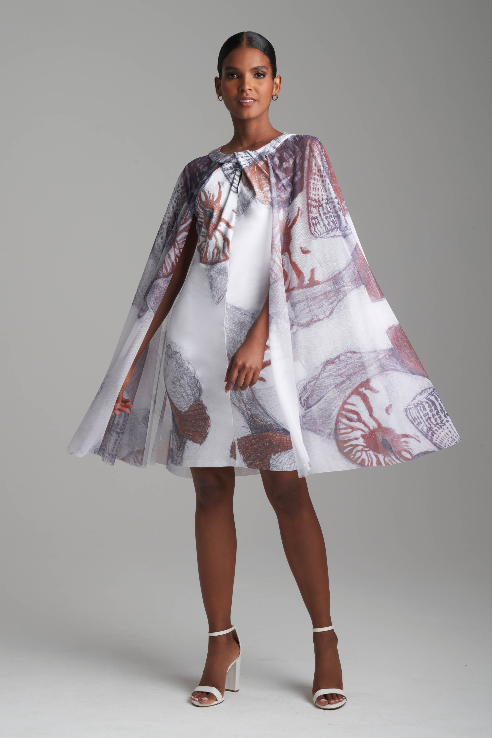 Woman wearing shell printed stretch knit dress with matching mesh cape attached by Ala von Auersperg