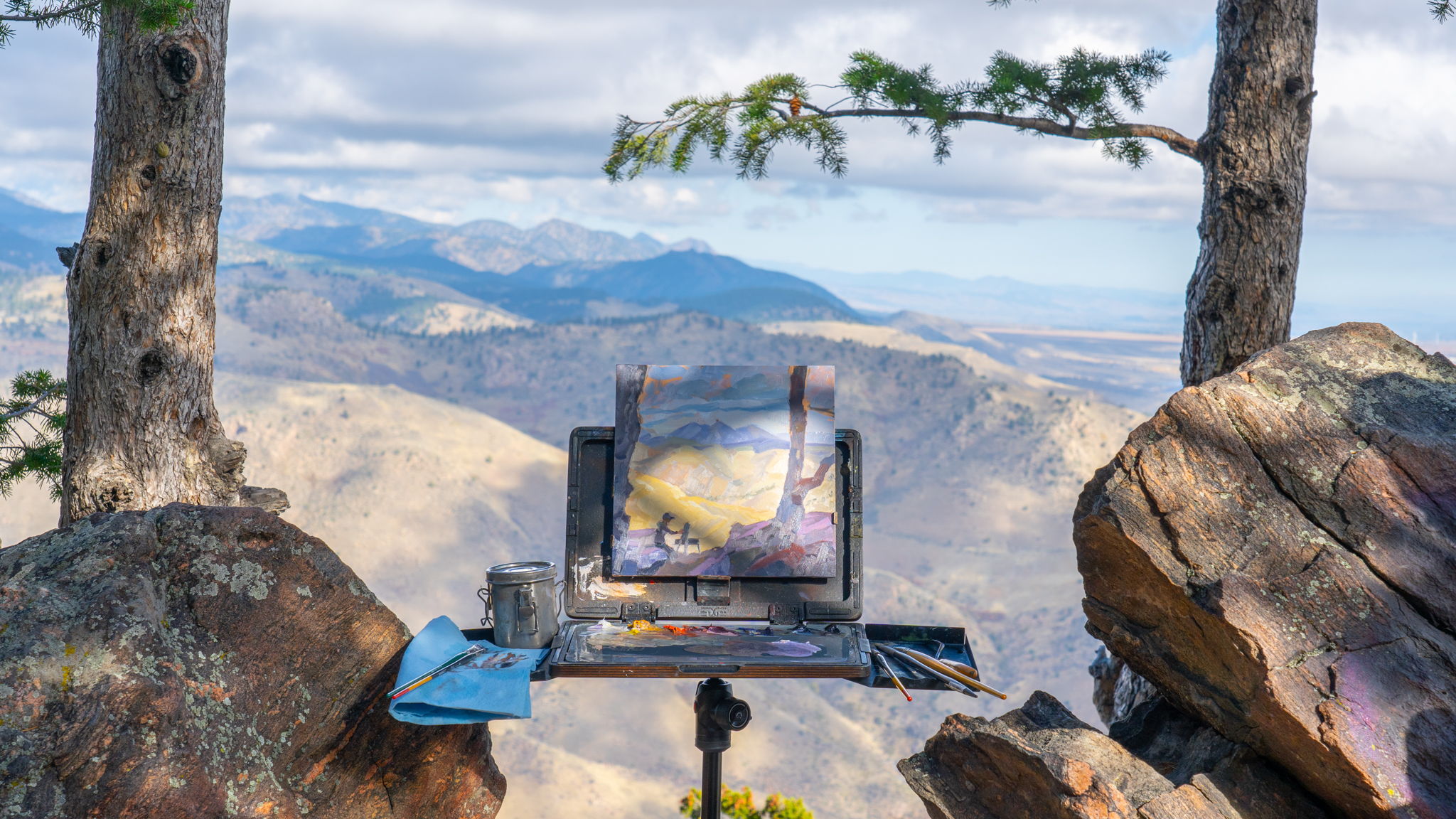 An easel with a painting overlooking a mountainous landscape.