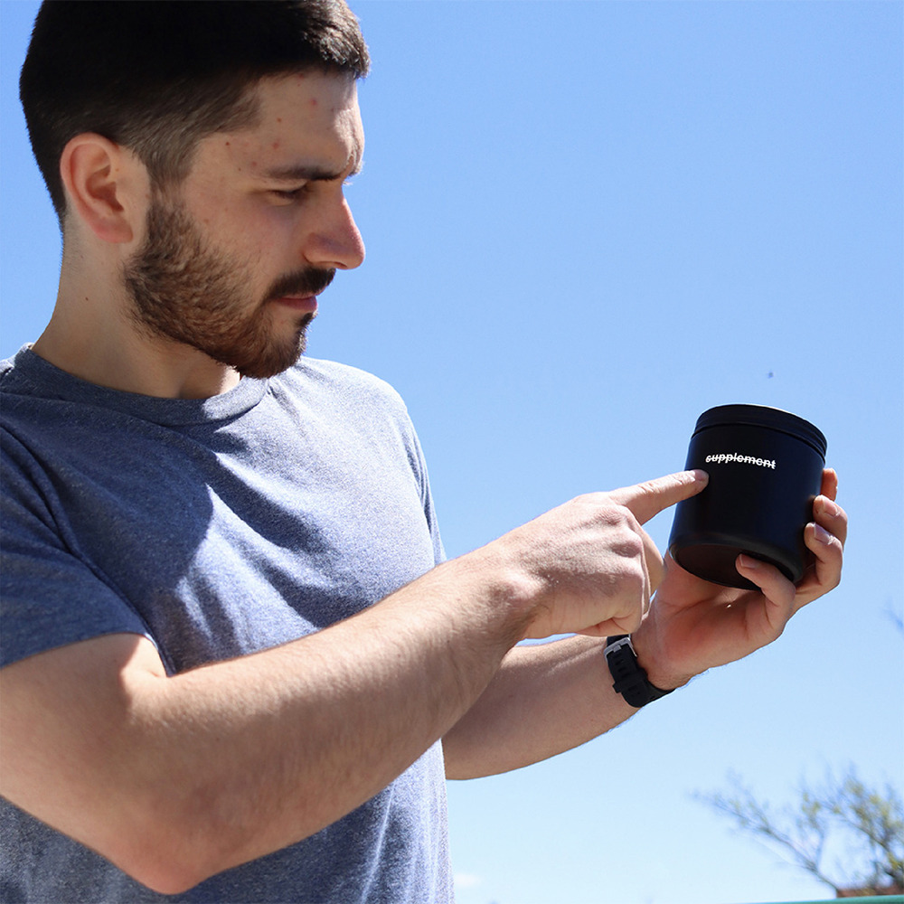 Man holding Complement Essential vegan multivitamin glass jar. 