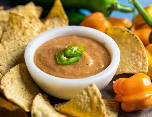 Bowl of dip surrounded by tortilla chips and fresh peppers.