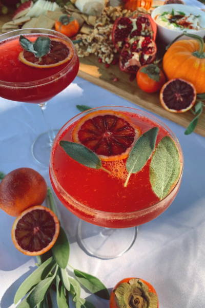 Blood orange mocktail in a coupe glass, surrounded by blood orange slices and pomegranate.