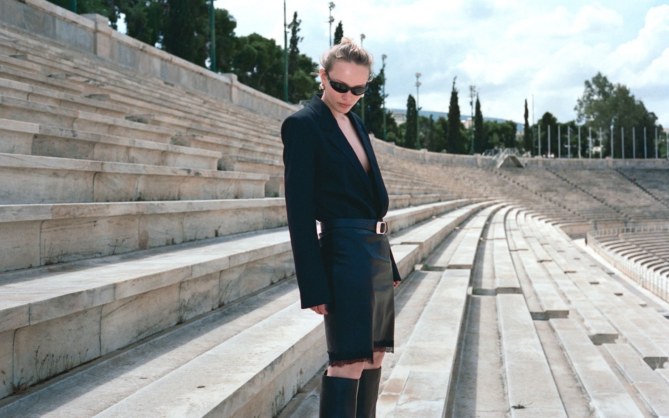 Person in a stylish outfit poses on stadium steps under a clear sky.