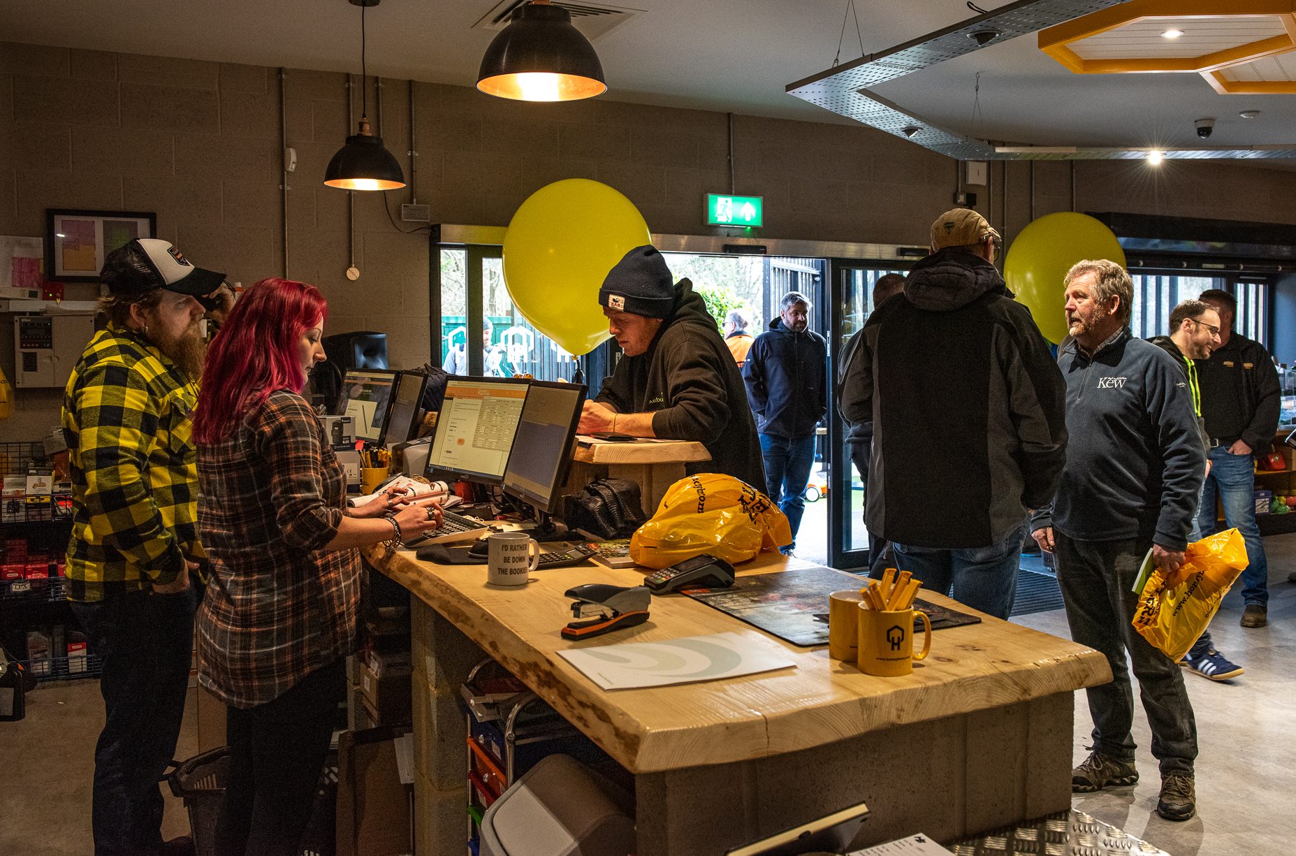 People interacting at a counter in a cozy indoor space with yellow balloons.