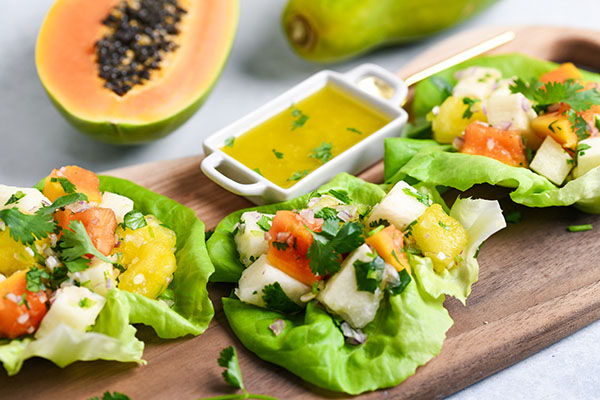 Three lettuce wraps with fruit and herbs, surrounded by papaya and pear.
