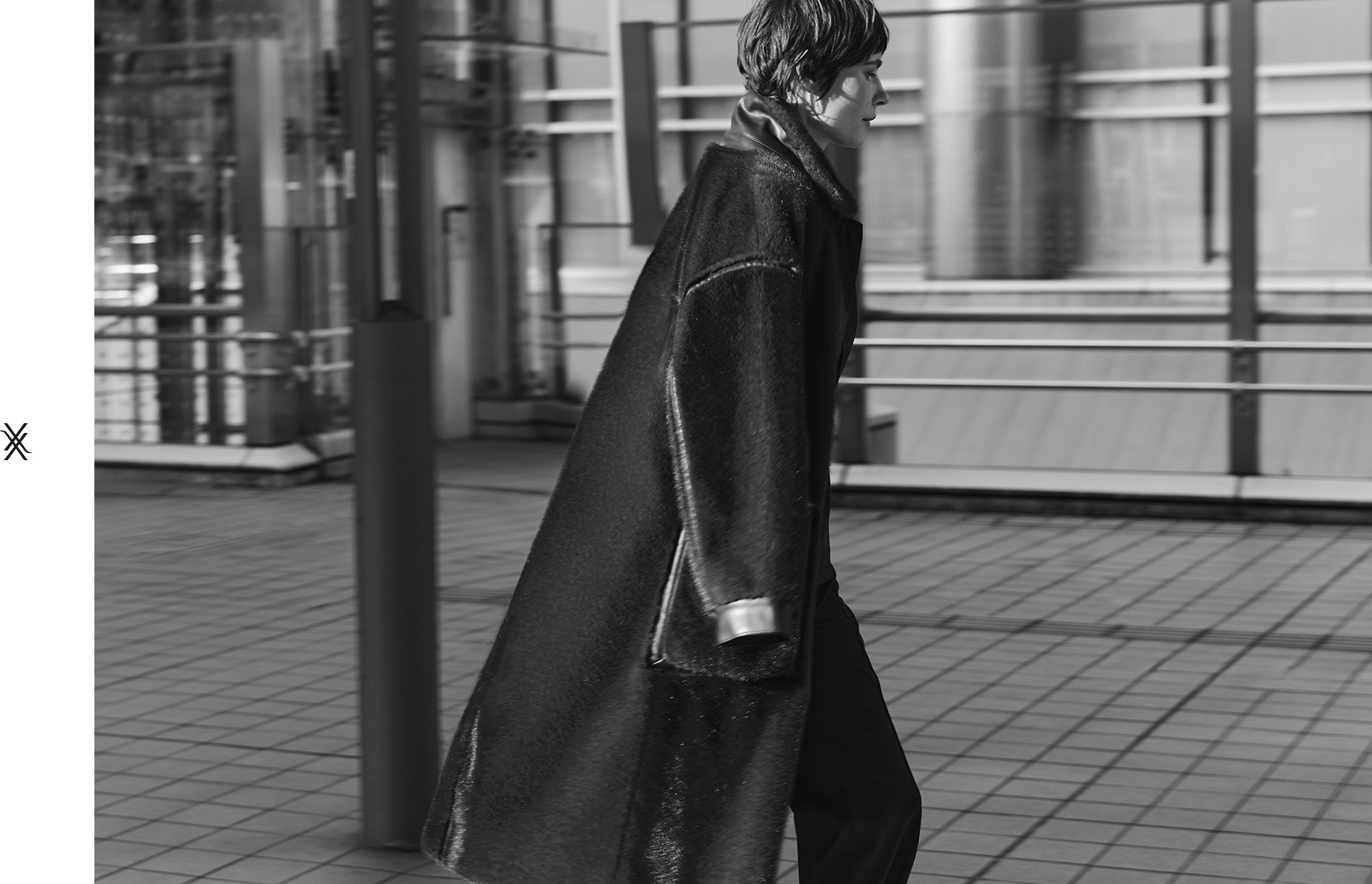Person walking in a long coat, with a city backdrop in black and white.