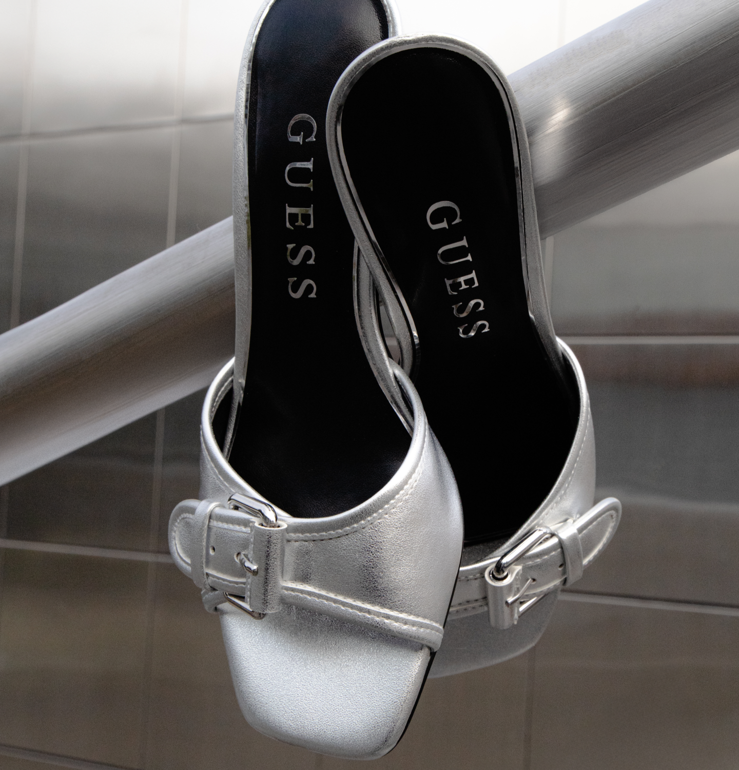Silver Guess Dista mules hanging on a railing.