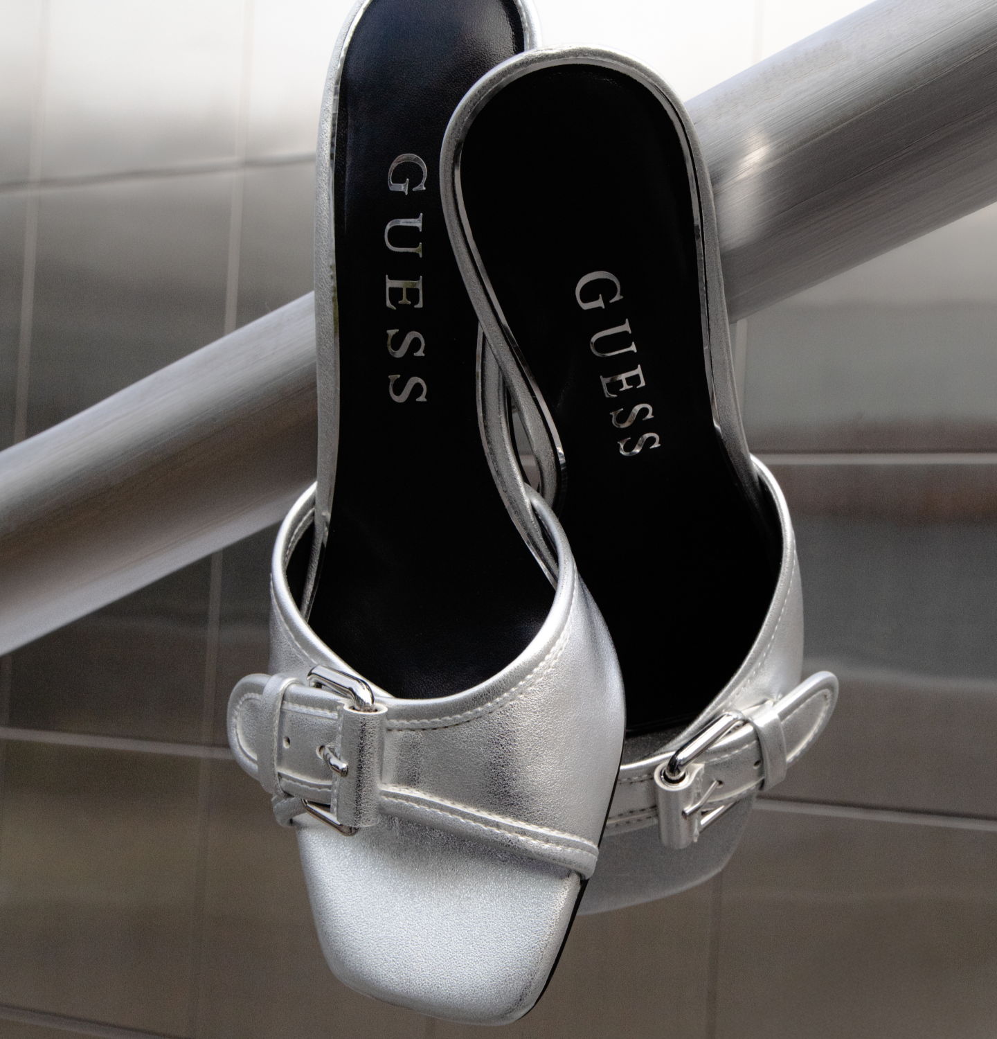 Silver Guess Dista mules hanging on a railing.