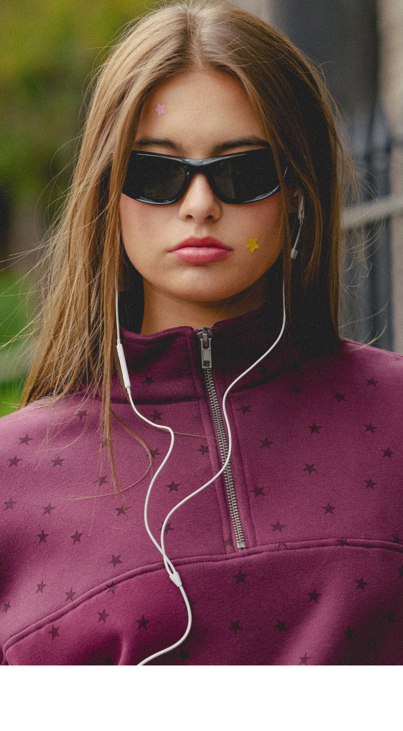 Young woman in sunglasses wearing a purple sweatshirt with headphones.