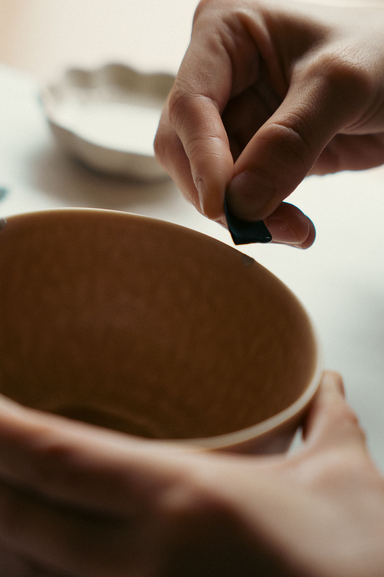 Person's hands placing an object into a ceramic bowl.