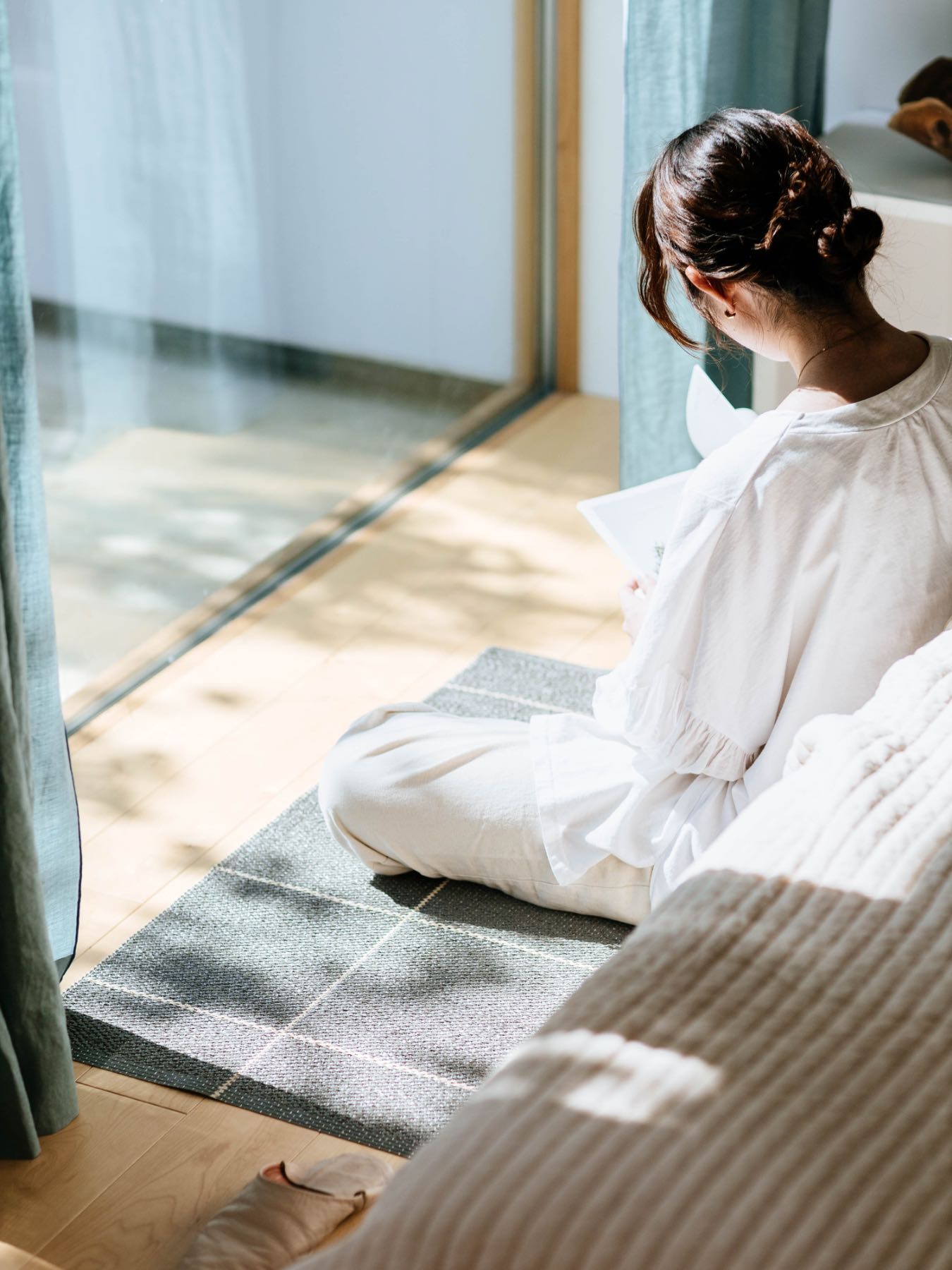 Person sitting on the floor, reading a book near a window.