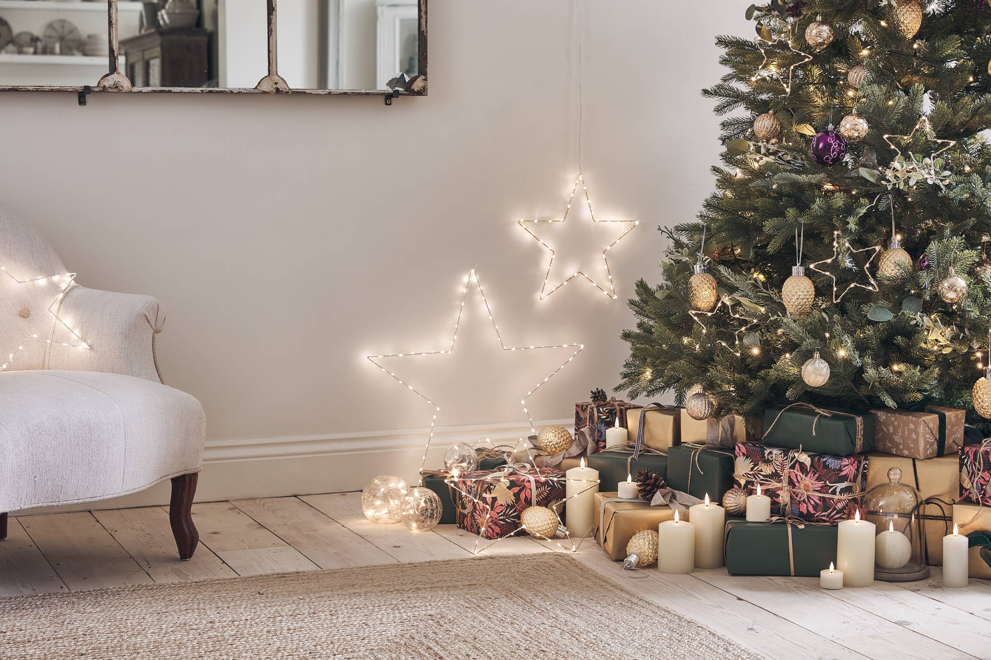 A Christmas tree dressed with golden baubles and star lights standing in a  cosy living room .