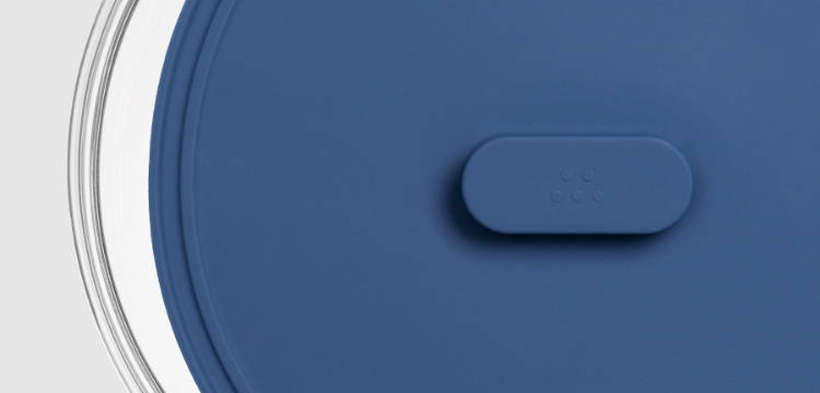 A Blue Misen Universal Lid with raised handle partially covering a glass food storage bowl.