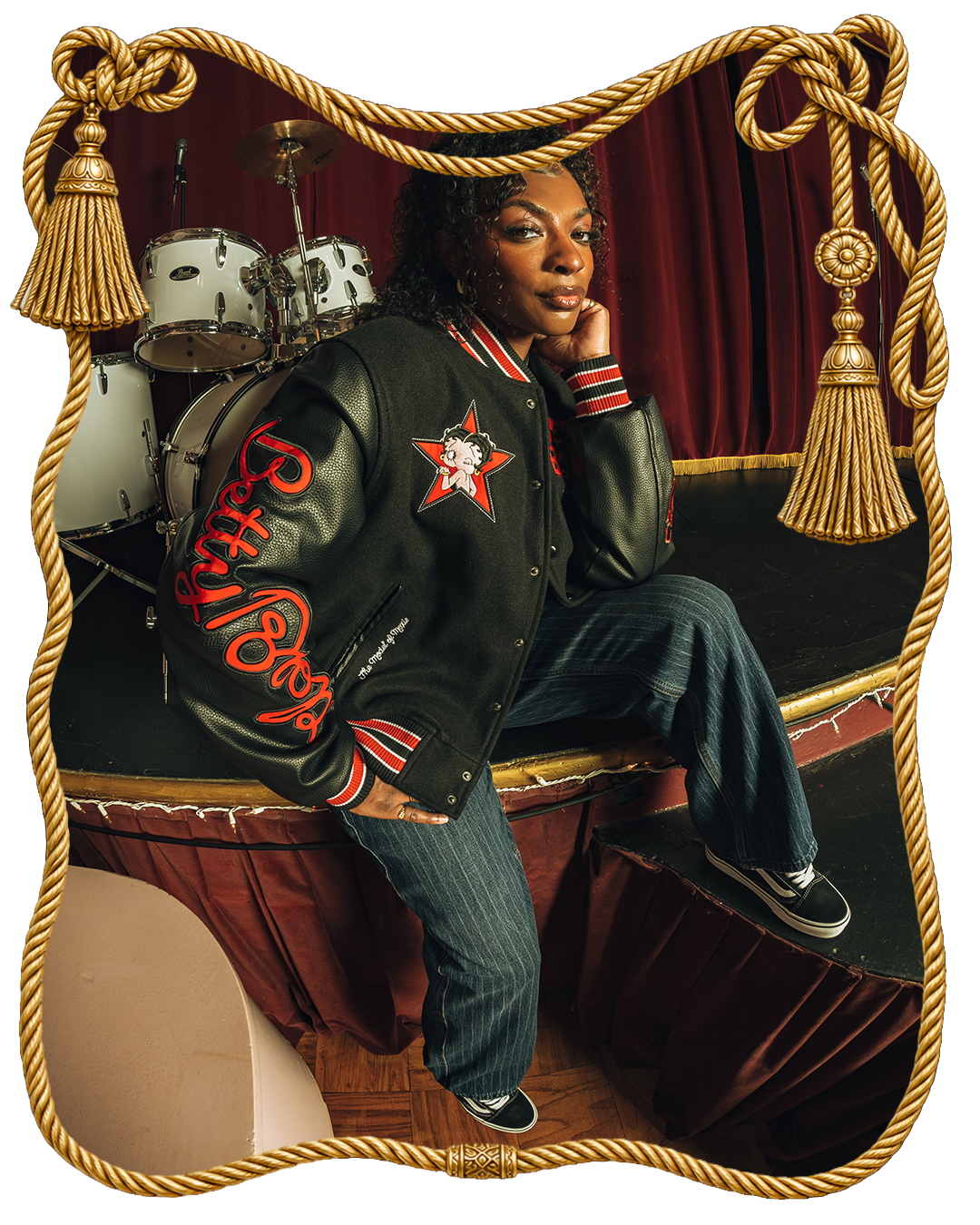 Person in a stylish jacket poses on stage with drums in background.