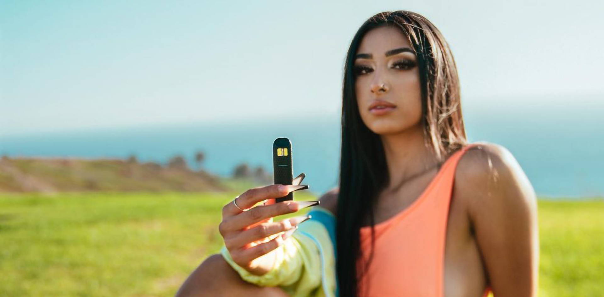 Influencer hold a vape disposable showing off clear concentrates on a cliff side