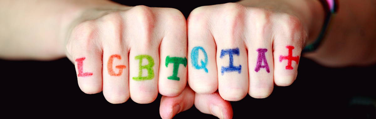 LGBTQIA+ letters written in rainbow letters on a persons fingers