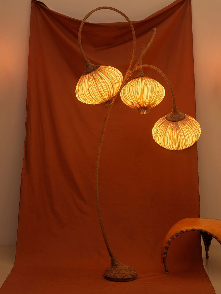 A stylish floor lamp with three curved shades against an orange backdrop.