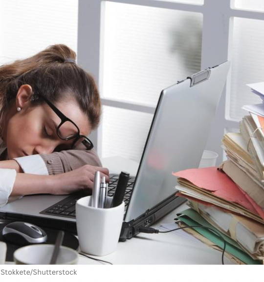 woman asleep at computer, desk piled with papers and folders, white pen holder, computer mouse