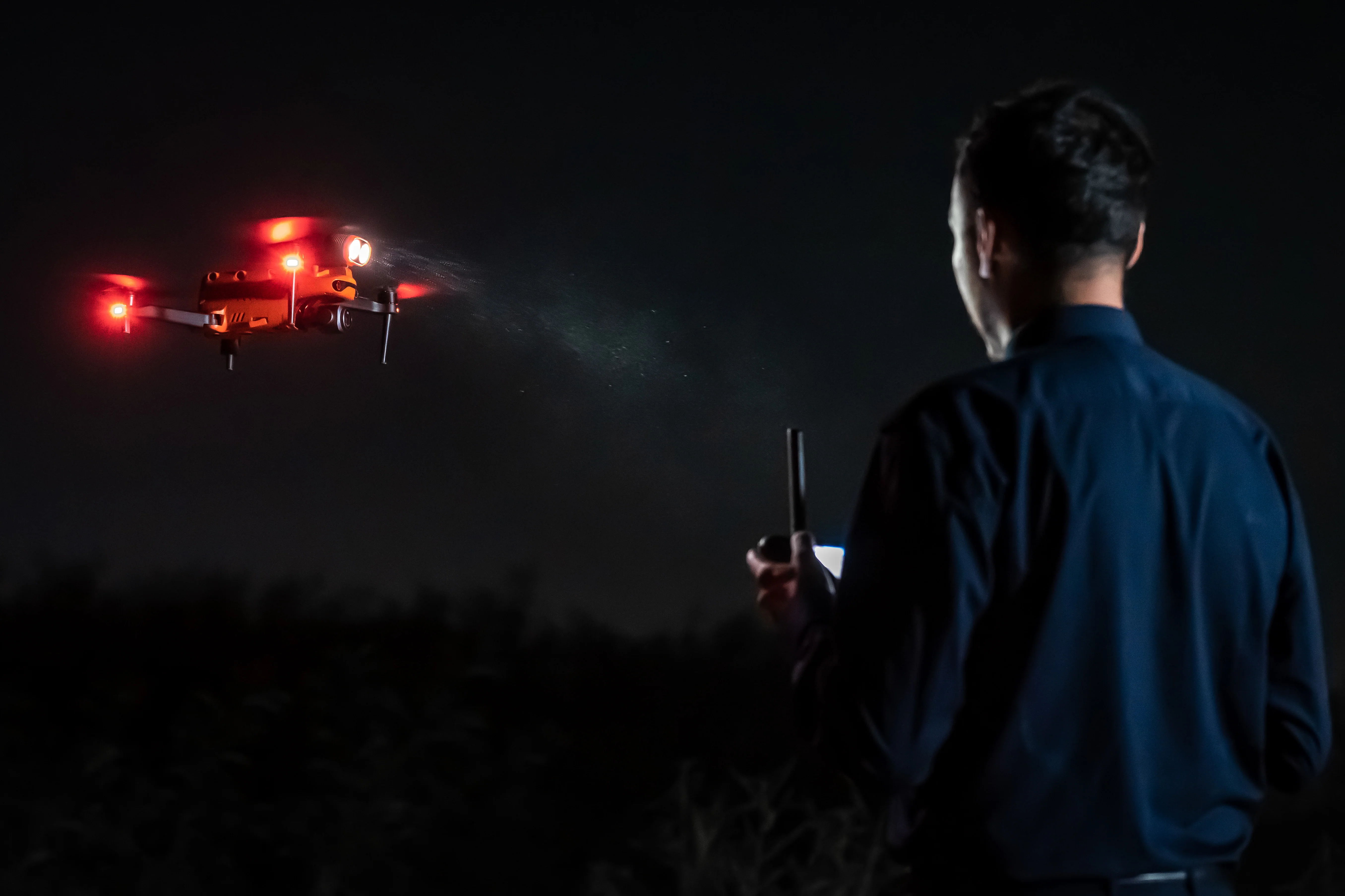 Person operating a drone at night with red lights.