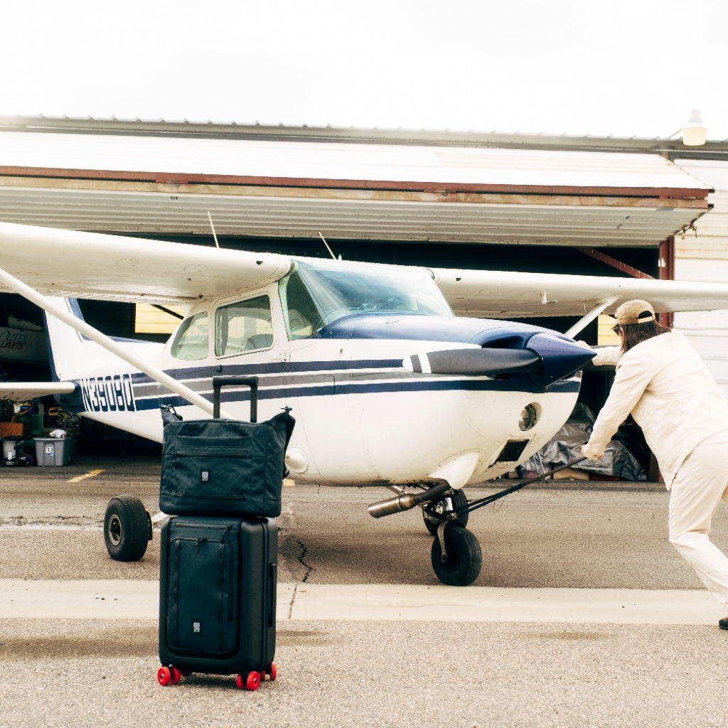 A person pushing a small airplane with luggage nearby.
