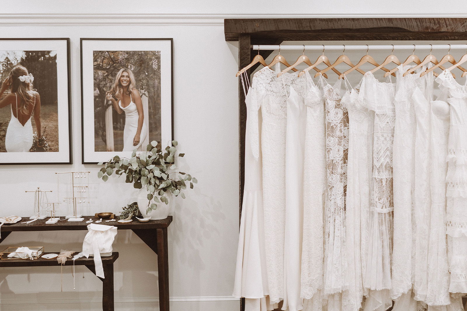 Bridal boutique display with dresses, framed photos, and a wooden table.
