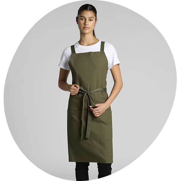 Model wearing an olive green denim bib apron with tie waist