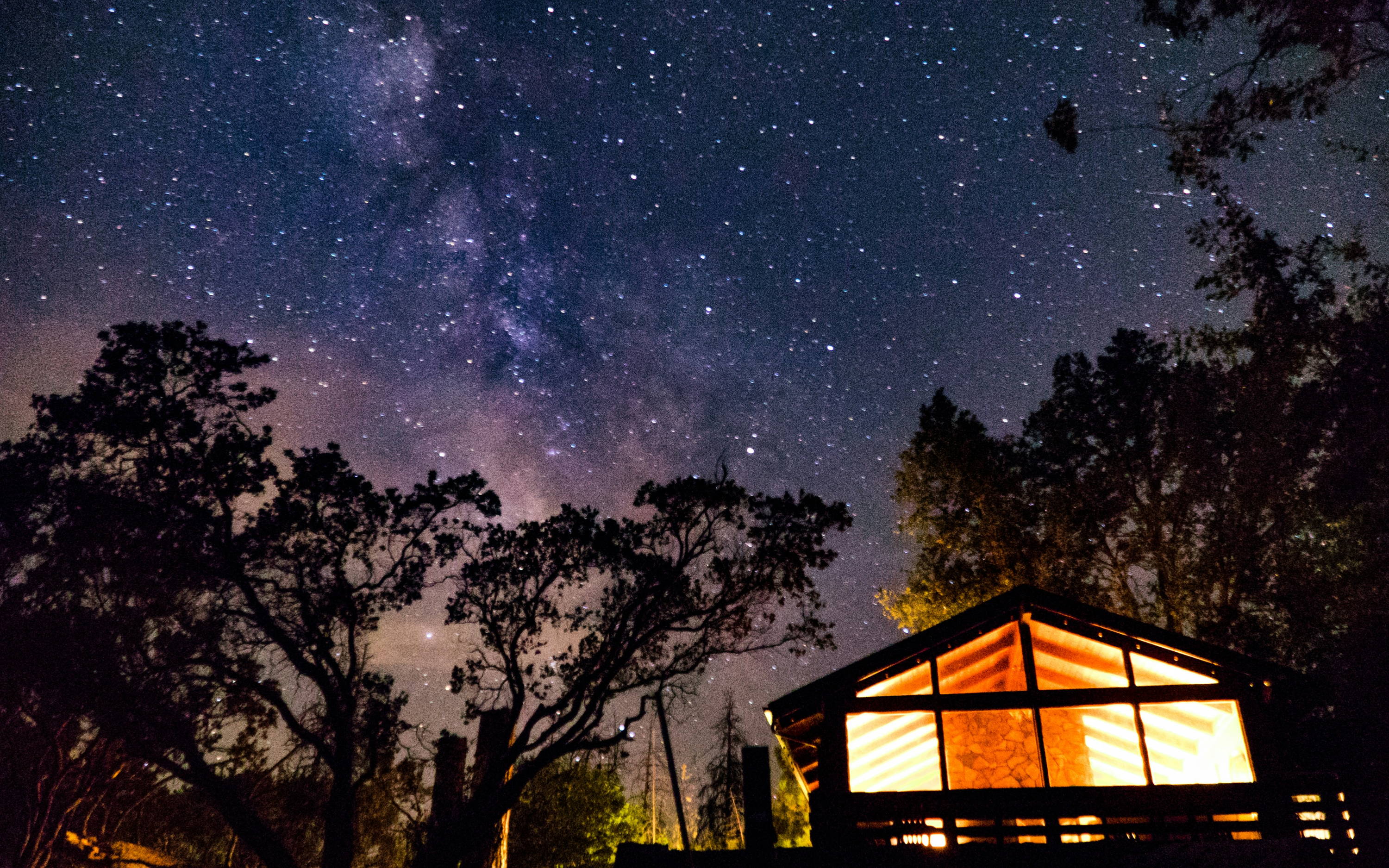 National park starry night sky in front of lit cabin.