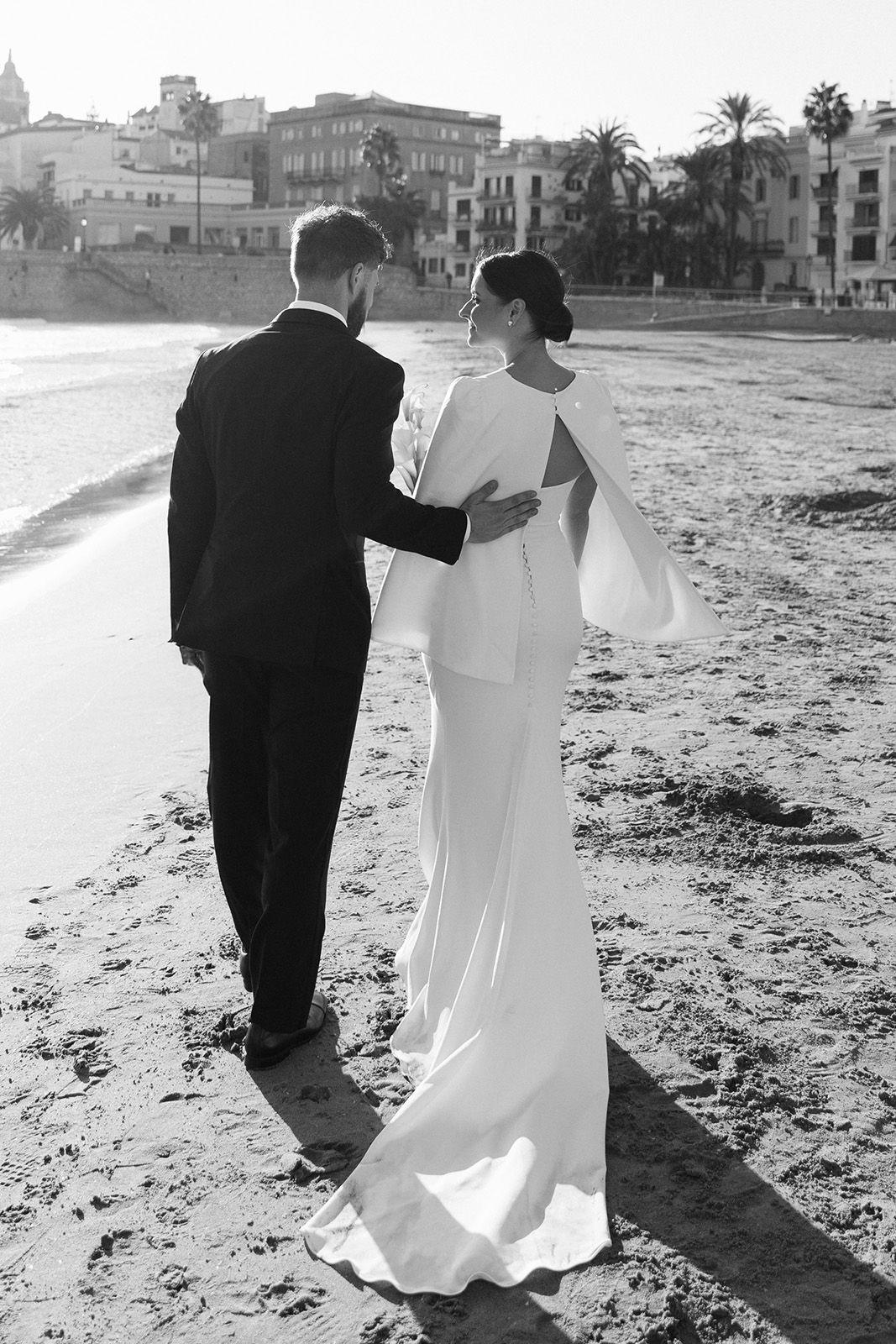 Couple walking on the beach in wedding attire, black and white photo.