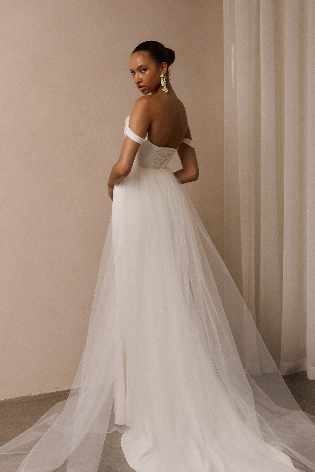 Woman in a white gown, facing away, with flowing fabric and elegant hairstyle.