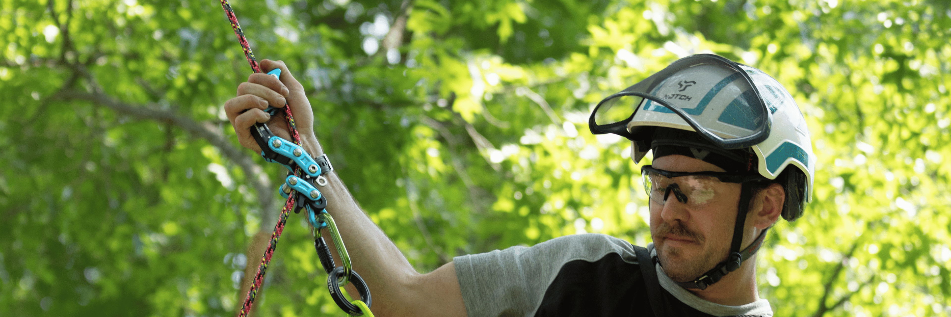 Person in helmet handling climbing gear in a forested area.