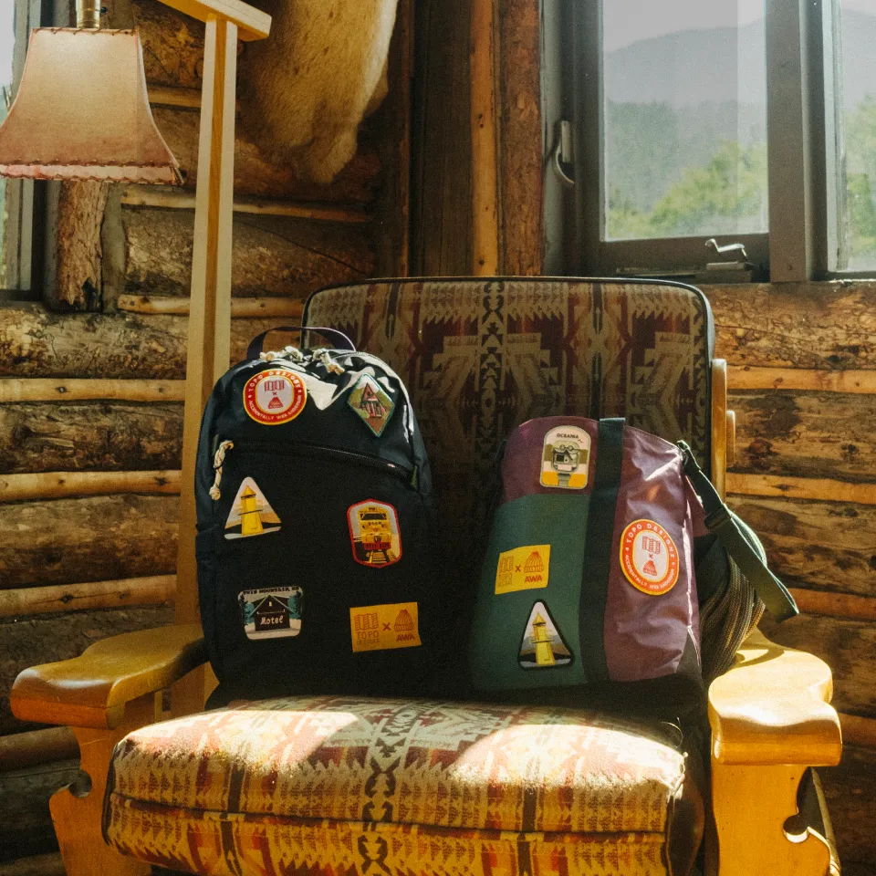 Two backpacks with stickers on a chair in a rustic cabin.