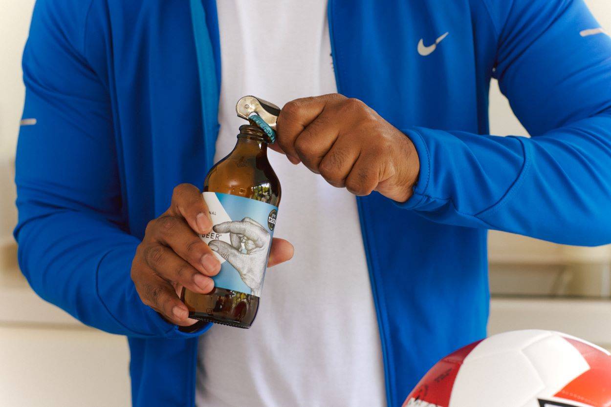 Young adult male wearing a training top opens a bottle of craft beer after exercise