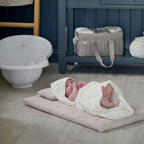 A swaddled baby lying on a mat in a nursery setting.