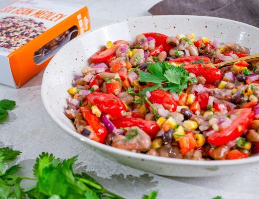 Bowl of colorful salad with tomatoes, corn, and herbs, next to packaging.