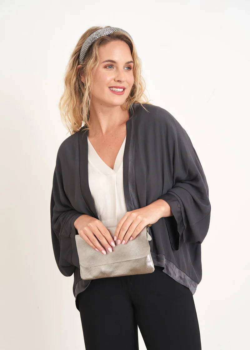 A model wearing a dark grey satin kimmono over an off white top and holding a grey clutch bag
