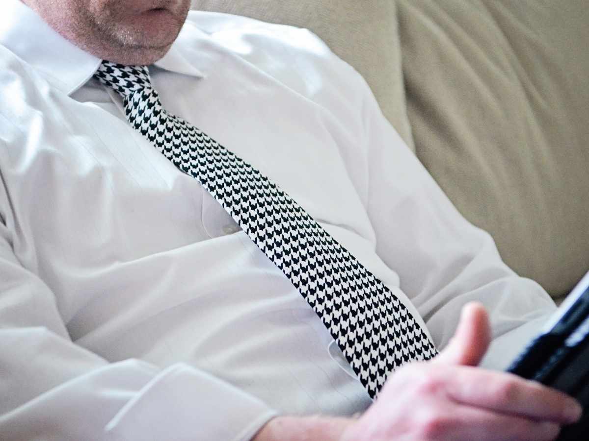 Man wearing a houndstooth necktie while lounging on a couch.