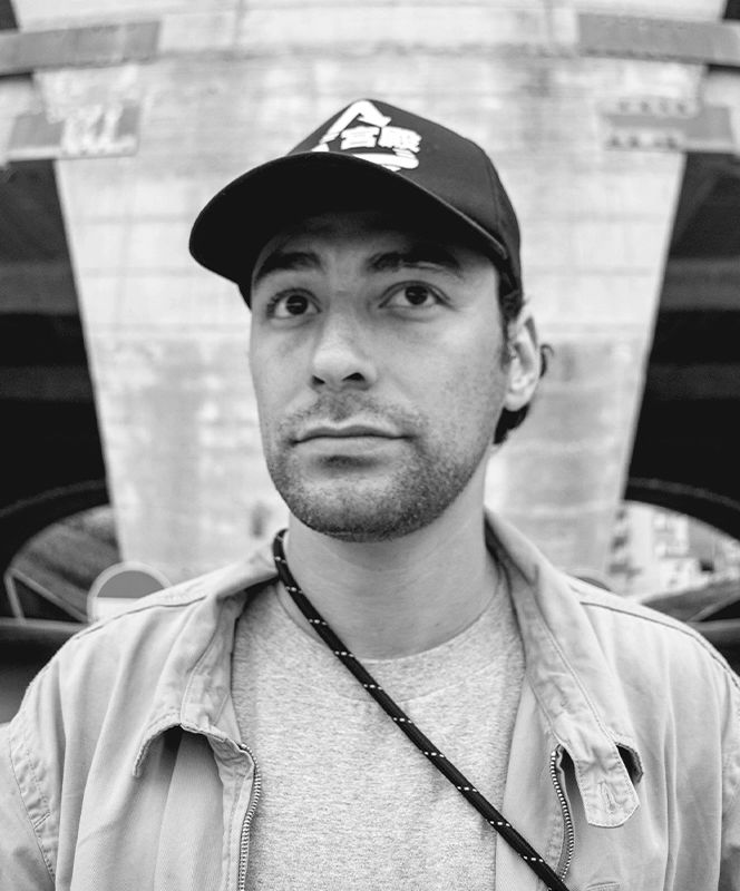 A man in a cap stands against a textured background.